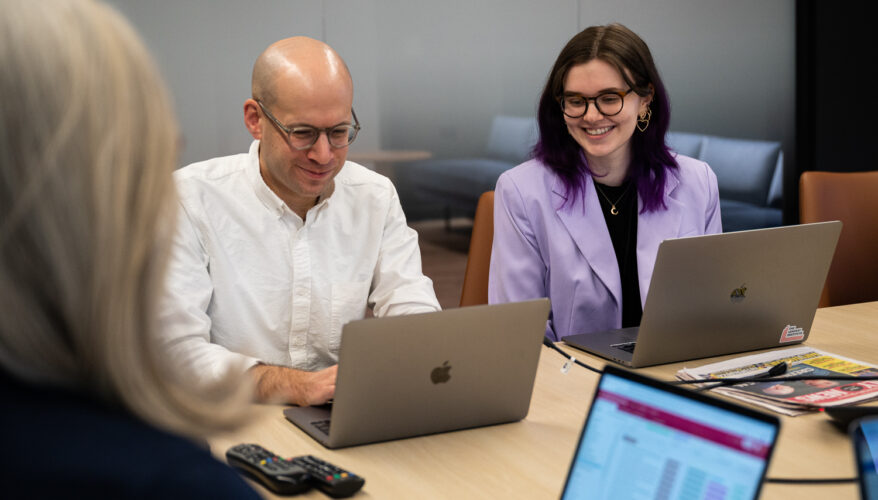 A bald man and a woman in a purple sport coat working around a conference table