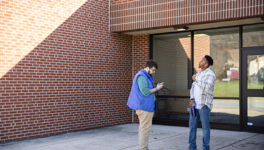 Spotlight PA Capitol Reporter Stephen Caruso, wearing a blue vest, speaks with a voter outside a polling place.