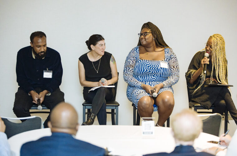 Four panelists sit on stools holding a discussion