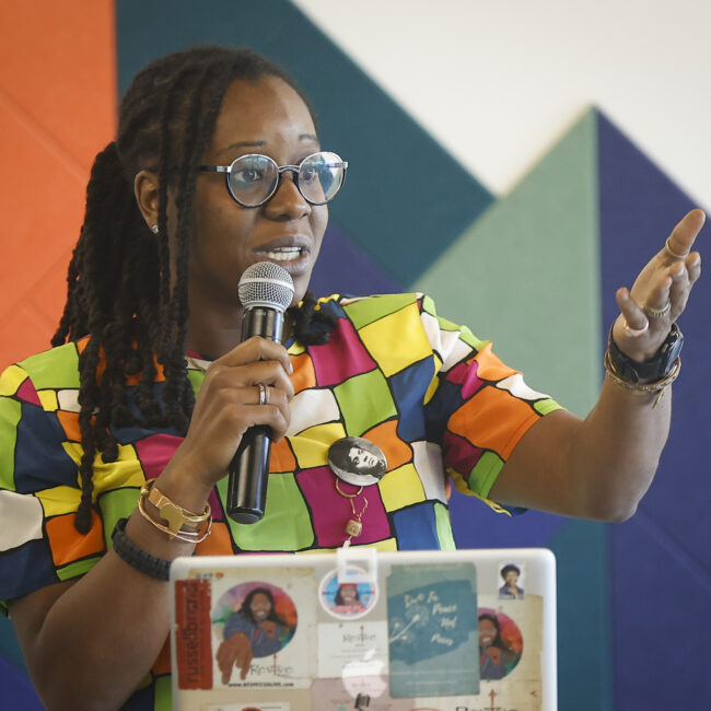 A woman in a colorful shirt speaks into a microphone