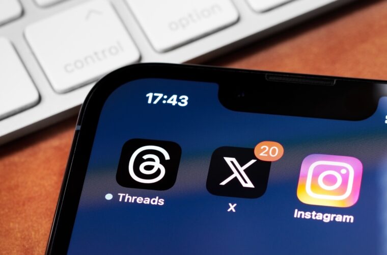 An iPhone showing the app icons for Threads, X (formerly Twitter), and Instagram