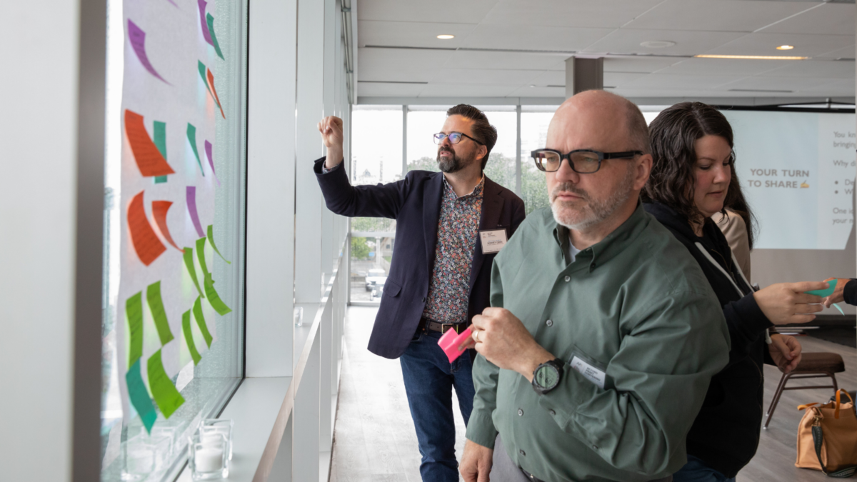 Two men place post-it notes on big sheets of paper.