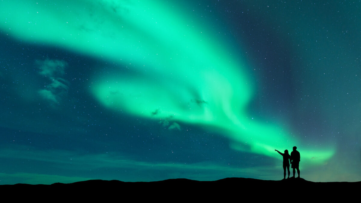 Two people stand beneath the northern lights.