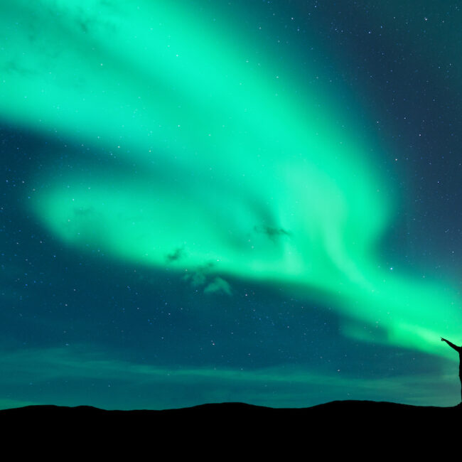 Two people stand beneath the northern lights.