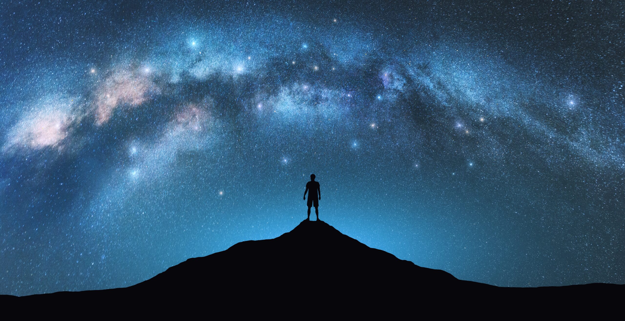 A person stands on a mountain beneath a starry sky