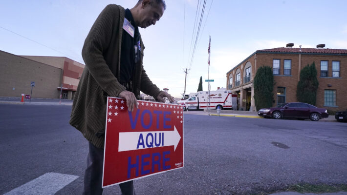 An election worker places a sign that says "Vote here/aqui" outside a polling station at a fire station in El Paso, Texas.