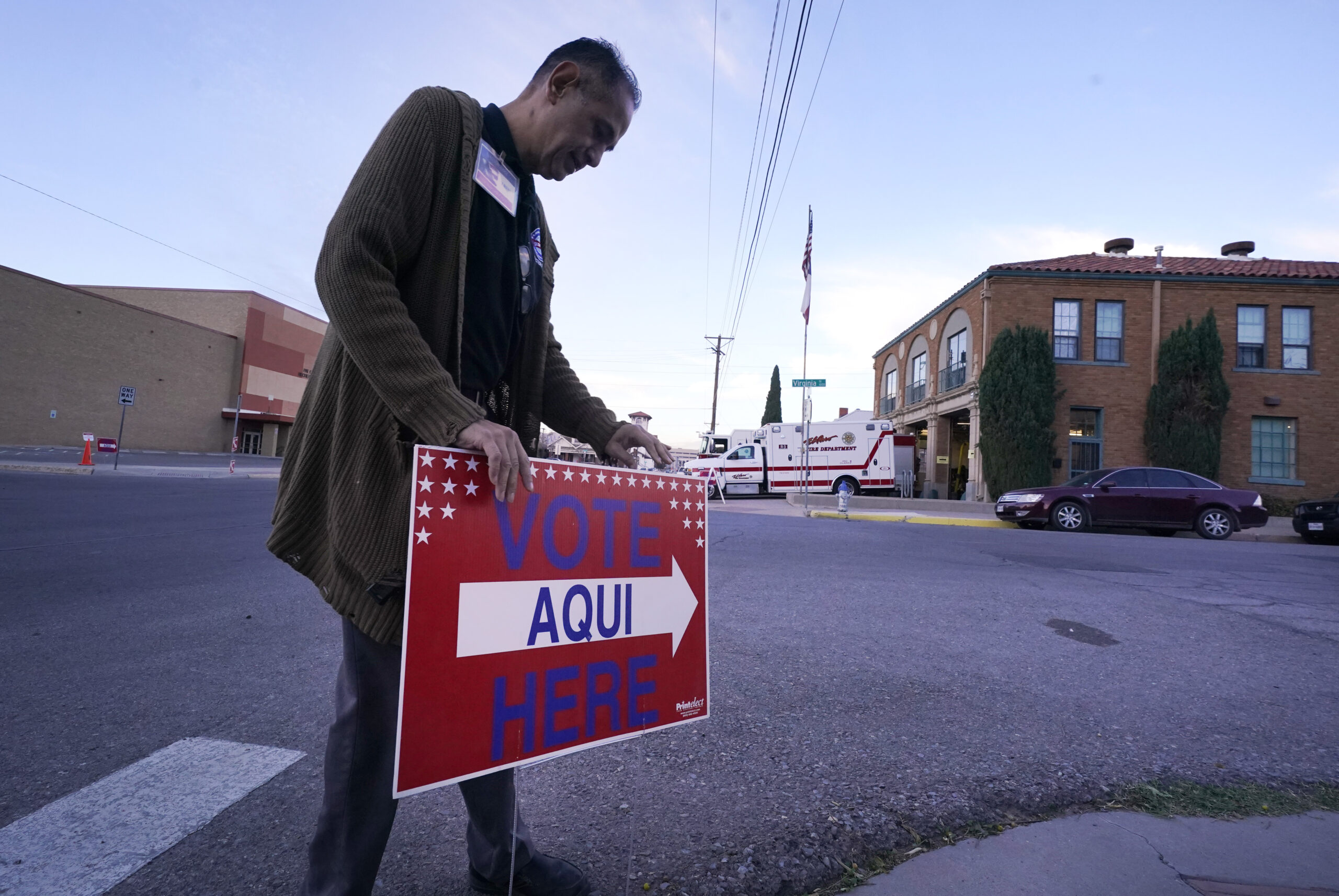 An election worker places a sign that says "Vote here/aqui" outside a polling station at a fire station in El Paso, Texas.